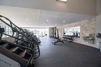 A gym with a row of treadmills on the left and a bench with weights on the right.at Linc, Des Moines  